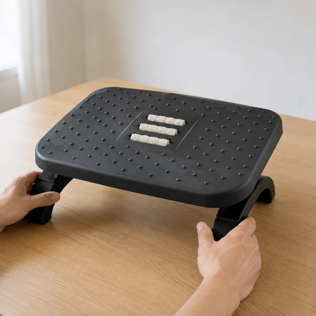 Mains ajustant l’inclinaison du repose-pied ergonomique posé sur une table en bois